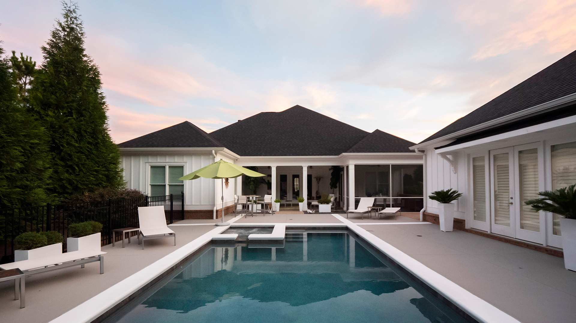 A large white house with a black roof and a rectangular swimming pool in the foreground